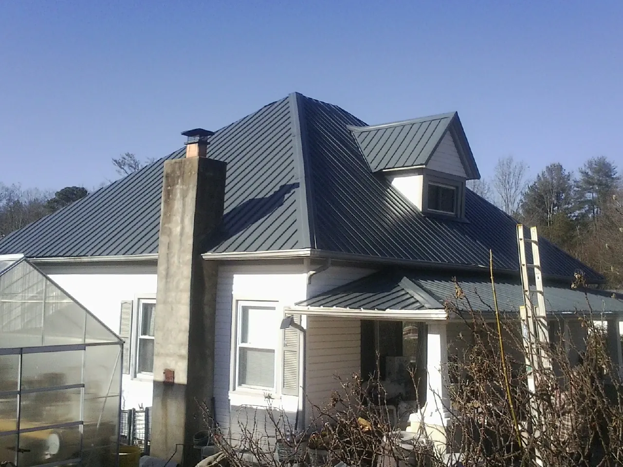 Dark blue standing seam metal roof on a white farmhouse with dormer — Slate & Tile Roof Repair by Roofing Brothers in Beatty