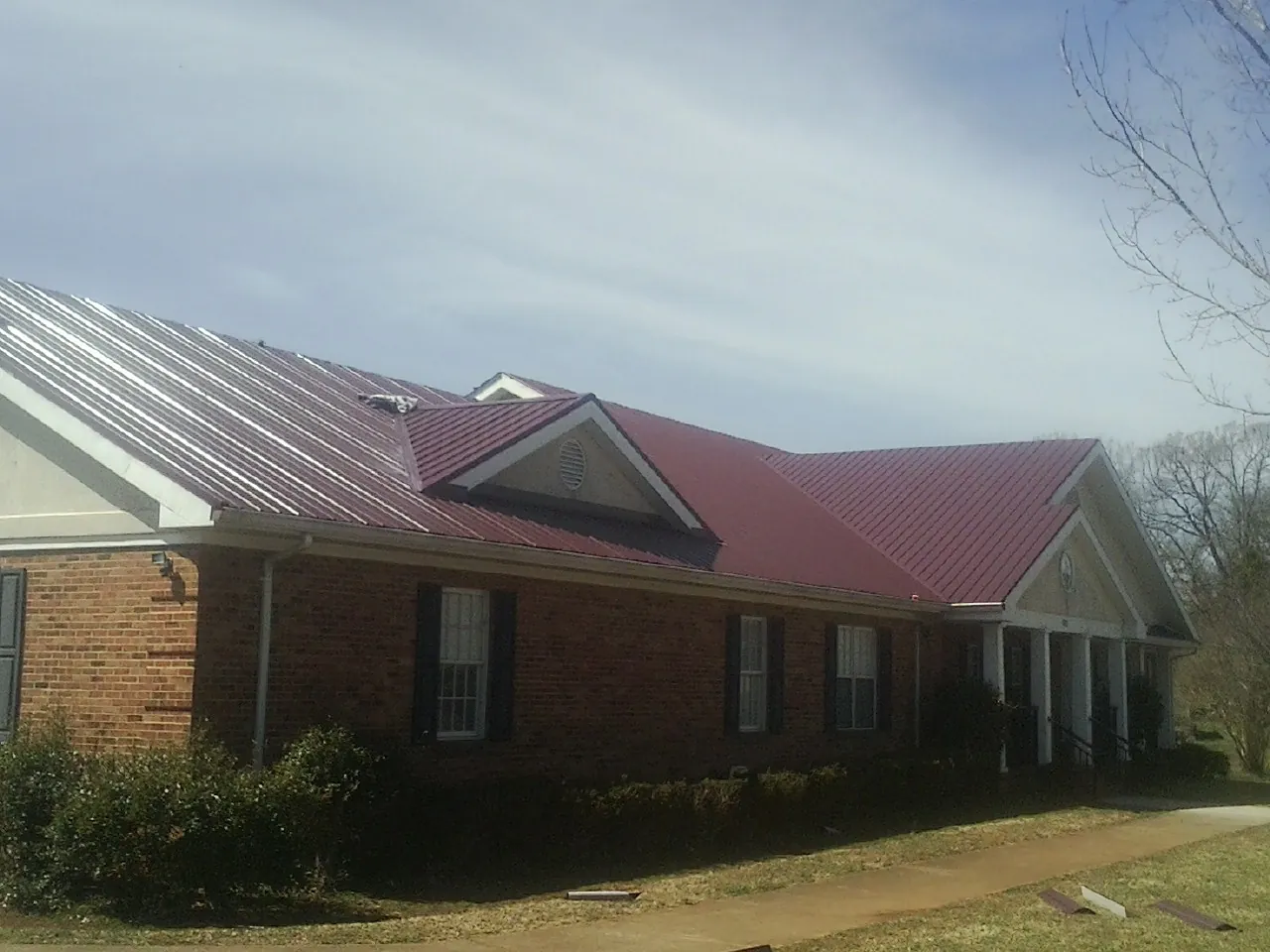 Red metal roof with gabled entries on a long brick building, from a Hail Damage Roof Repair job in Beatty