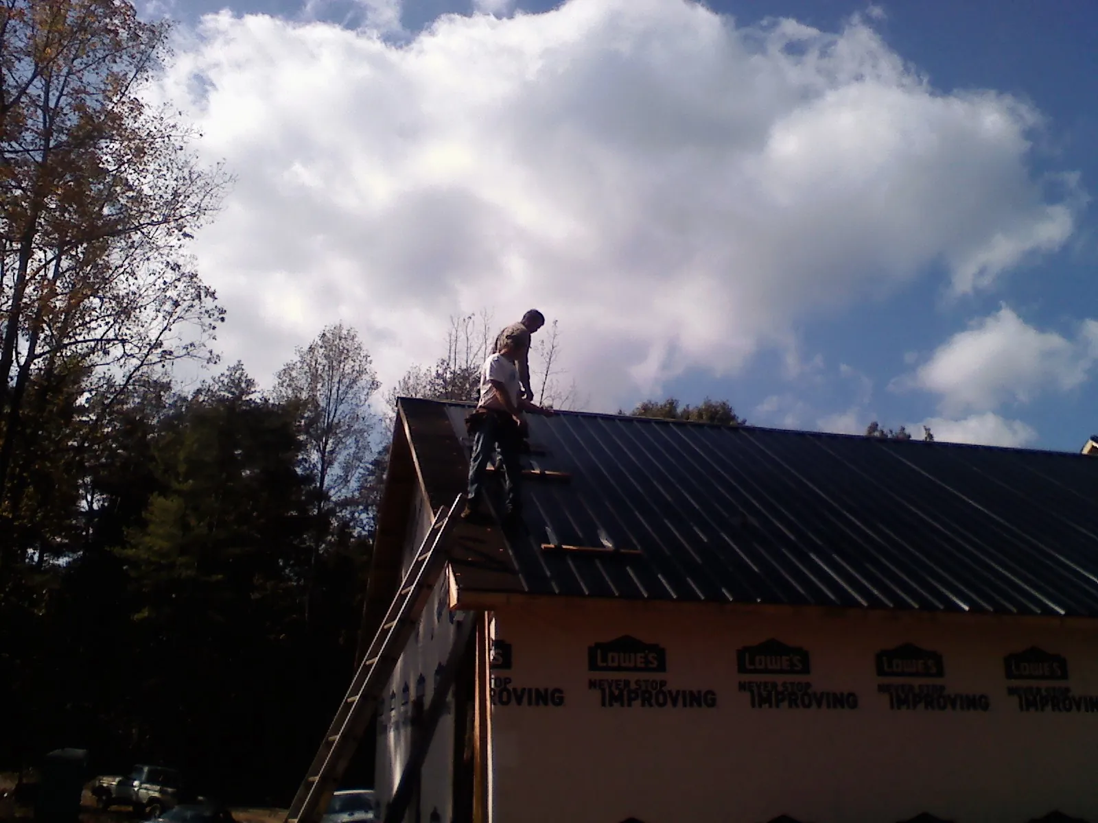 Roofer fastening dark metal panels high against a cloudy sky, from a Roof Inspection job in Beatty