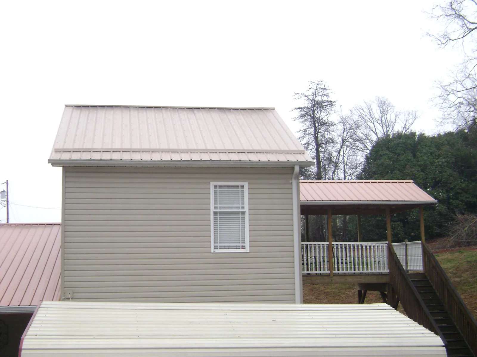 Tan metal roofs on a two story addition and attached porch, from a Roof Replacement job in Beatty